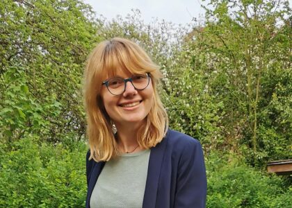 Julia Fink lächelt und steht in einem Garten hinter einem Hochbeet mit grünem Mangold.