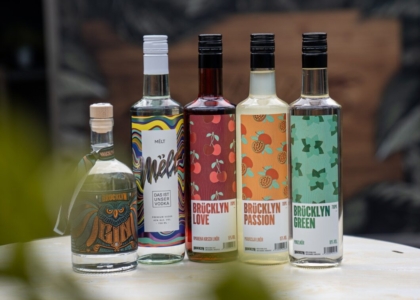 Fünf Flaschen Spirituosen nebeneinander auf einem Tisch, darunter Gin, Wodka und Liköre mit folgendem Schriftzug: Brücklyn und Mēlt.