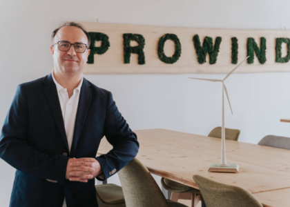 Mann im Sakko steht im Büro neben einem Tisch mit Windrad-Modell und dem Schriftzug „PROWIND“ an der Wand.