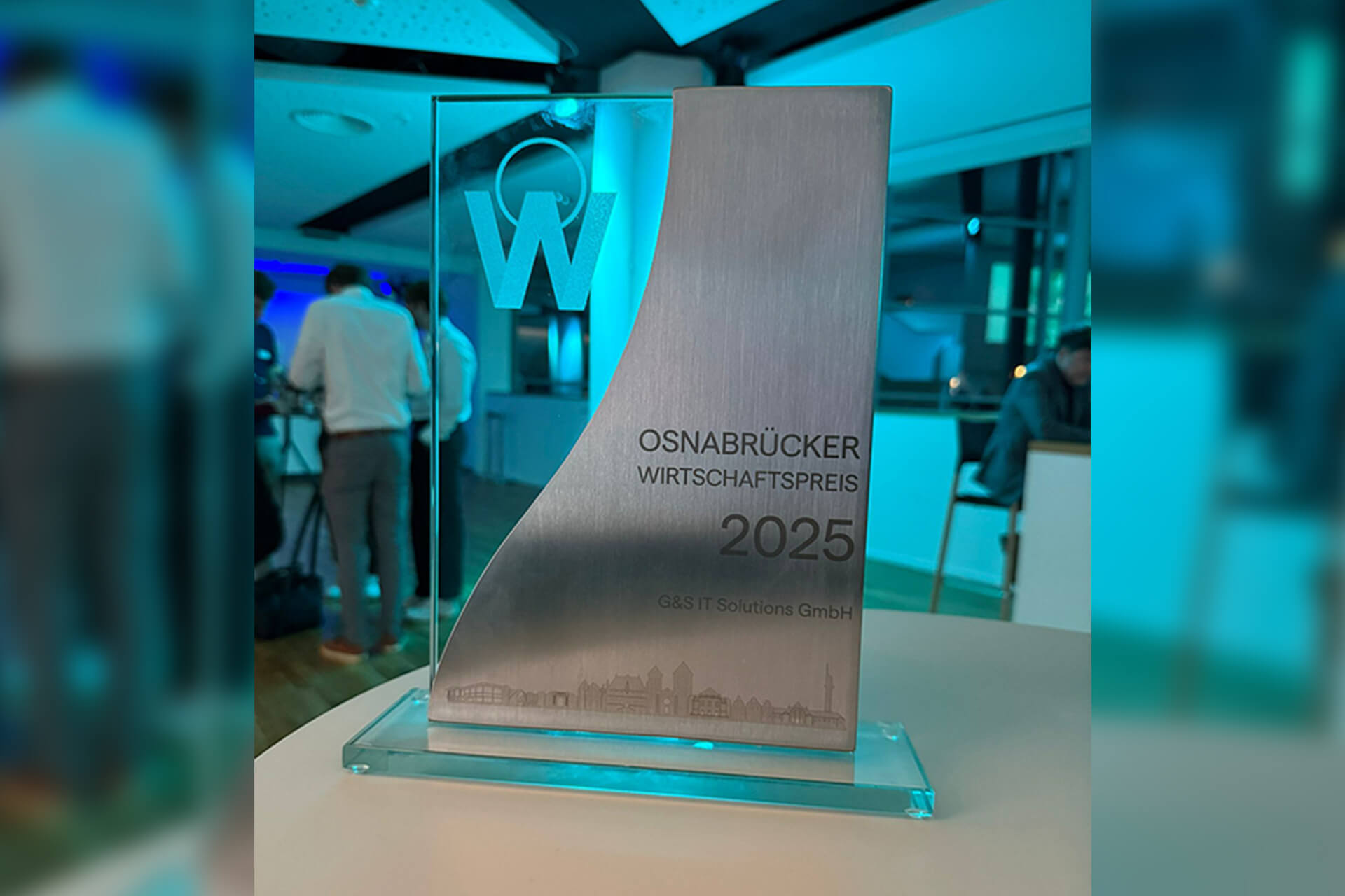 Eine moderne Glastrophäe des Osnabrücker Wirtschaftspreises 2025 steht beleuchtet auf einem Tisch.