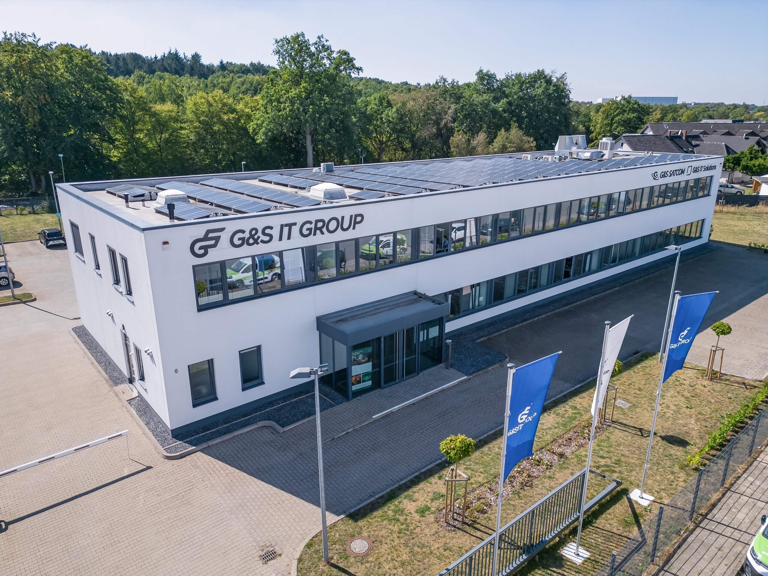 Außenansicht des zweigeschossigen Firmengebäudes der G&S IT Group mit Solaranlage auf dem Dach und blauen Flaggen.
