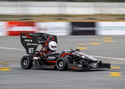 Ein Rennfahrer mit weißem Helm fährt mit einem schwarzen Formel-Rennwagen dynamisch über eine Teststrecke.