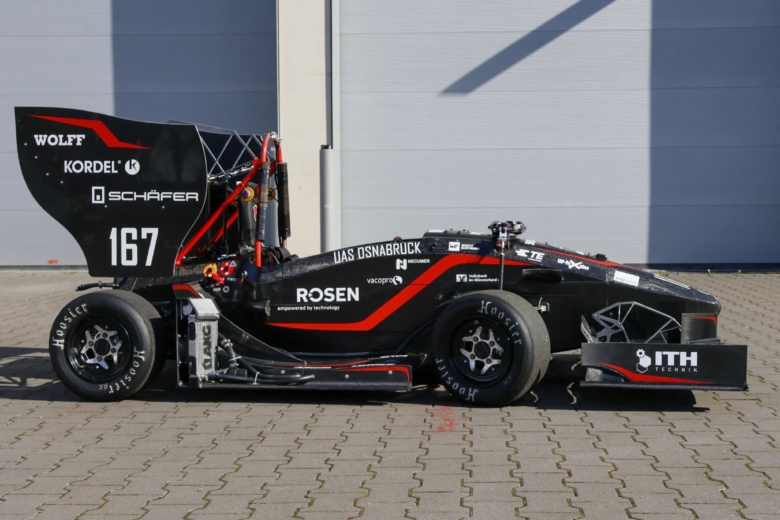 Ein schwarz-roter Formel-Rennwagen des Ignition Racing Teams steht in der Seitenansicht auf einem Pflasterplatz.