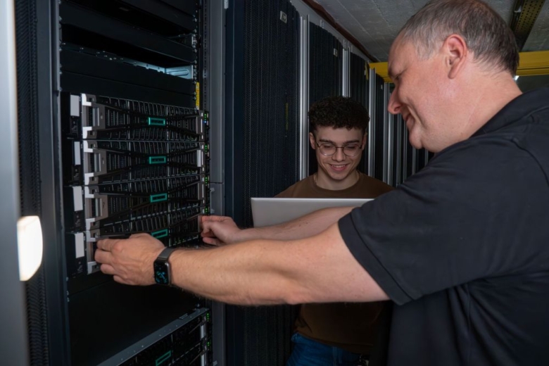 Zwei Mitarbeiter der SIEVERS GROUP vor einem Serverschrank. EIner hält einen LapTop.