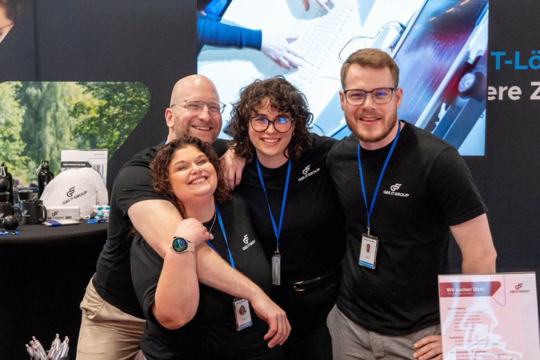 Vier Personen im Team-Outfit der G&S IT Group lächeln gemeinsam an einem Messestand.