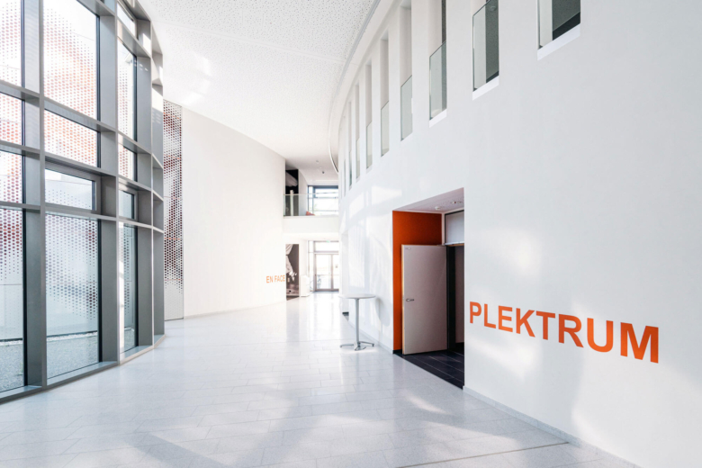 Heller, moderner Innenraum mit hoher Glasfront und orangefarbenem Aufdruck Plektrum an der Wand.