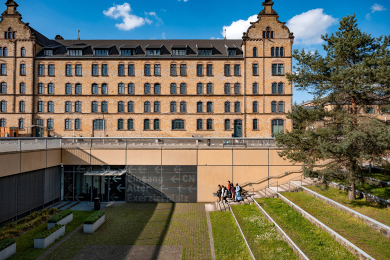 Historisches Sandsteingebäude mit großer Freitreppe im Vordergrund, auf der Personen gehen.