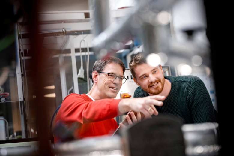Zwei Männer schauen aufmerksam auf eine Apparatur in einem technischen Labor.