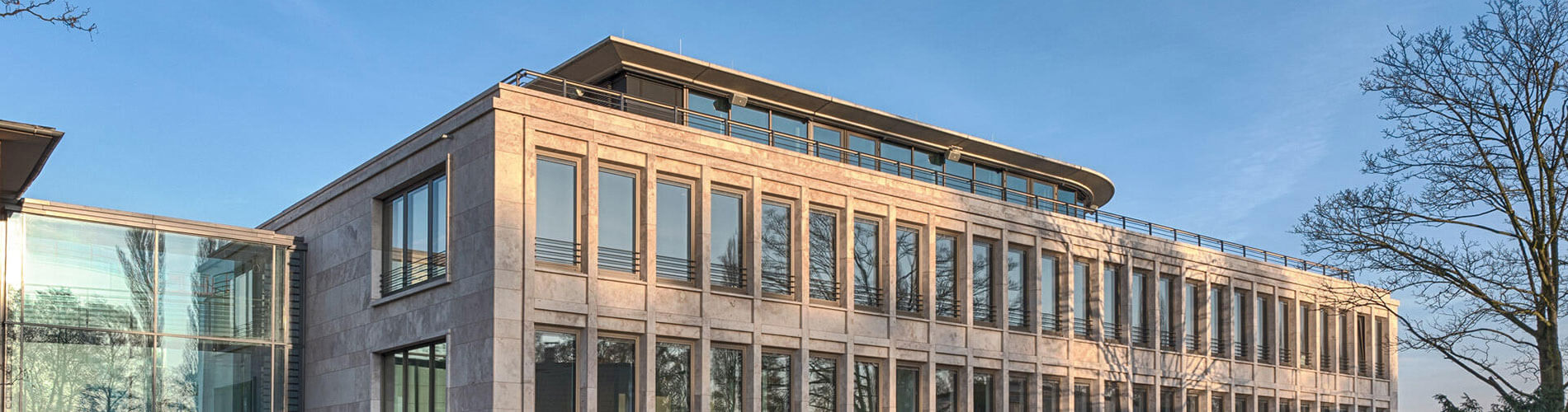 Modernes Bürogebäude aus hellem Naturstein mit Glaselementen und umlaufender Dachterrasse.