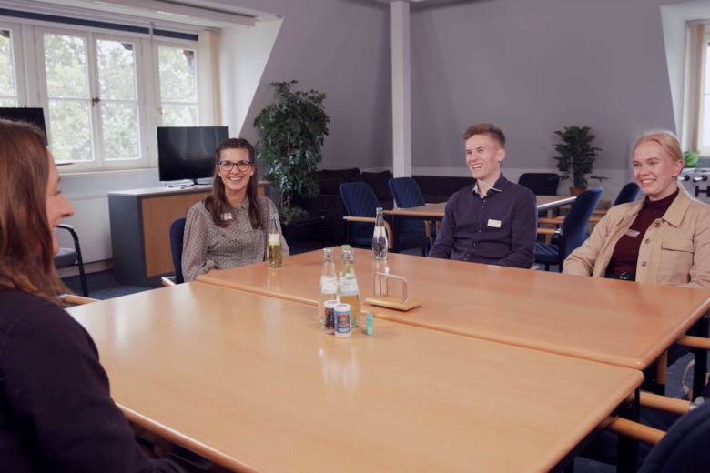 Vier Teammitglieder in einem modernen, hellen Besprechungsraum während eines freundlichen, lockeren Gesprächs.