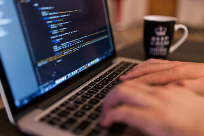 Hände tippen auf der Tastatur eines Laptops, auf dem Quellcode angezeigt wird.