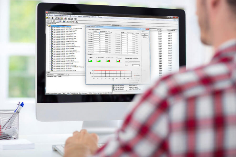 Rückansicht einer Person im karierten Hemd, die vor einem Monitor mit einer Datenverwaltungs-Software sitzt.