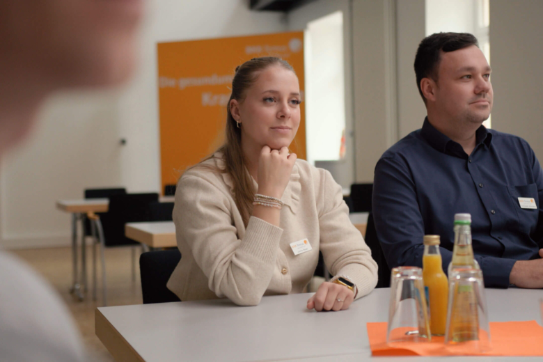 Eine Frau und ein Mann sitzen an einem Besprechungstisch und hören aufmerksam einem Gegenüber zu.