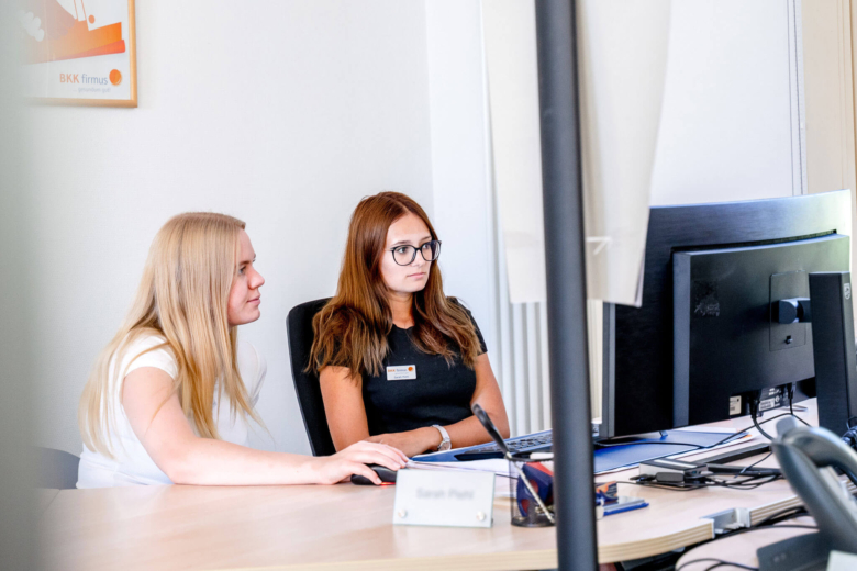 Zwei Mitarbeiterinnen der BKK firmus bei der gemeinsamen Arbeit am PC-Arbeitsplatz.