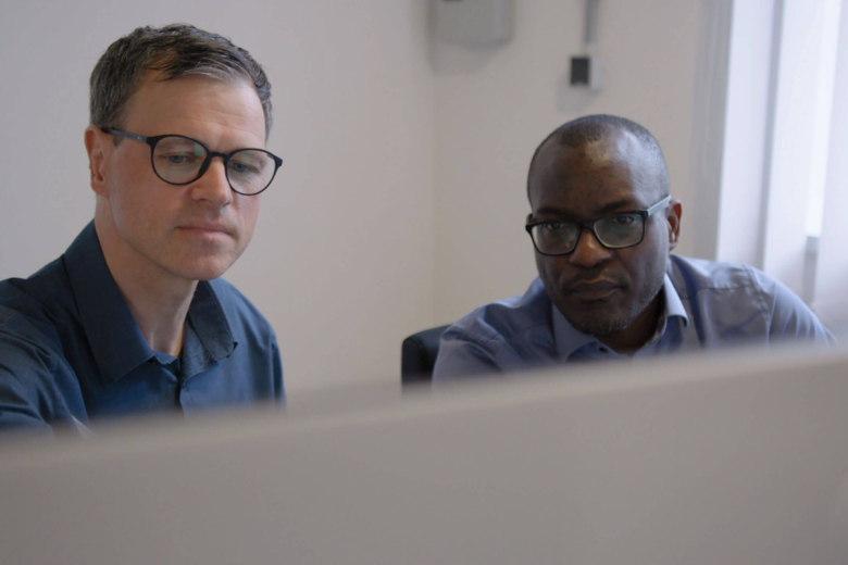 Zwei Männer mit Brille schauen gemeinsam aufmerksam auf einen Monitor außerhalb des Bildes.