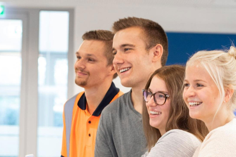 Vier lächelnde junge Bohnenkamp-Mitarbeitende schauen gemeinsam nach links, einer davon in Warnkleidung.