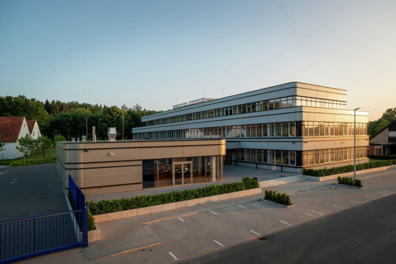 Modernes, mehrstöckiges Bürogebäude der Bohnenkamp AG mit hellem Anbau und Parkplätzen bei Sonnenschein.