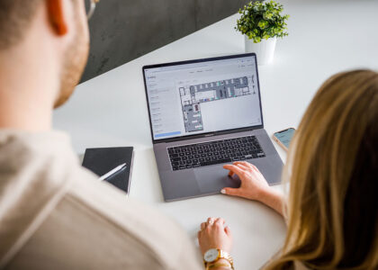 Zwei Personen blicken von oben auf einen Laptop, auf dem ein digitaler Büro-Grundriss zur Arbeitsplatzbuchung geöffnet ist.