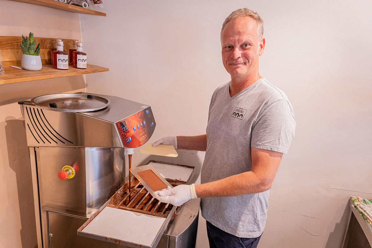 Ein Mann mit Handschuhen füllt flüssige Schokolade aus einer Temperiermaschine in eine Schokoladenform.
