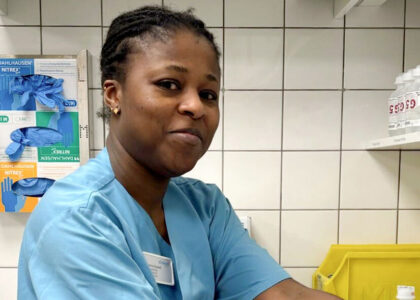 Dorcia Gyamfi in blauer Pflegekleidung im Krankenhaus- oder Praxisumfeld.
