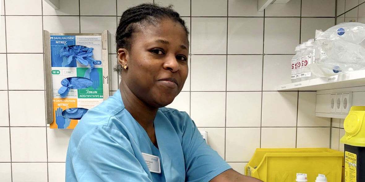 Dorcia Gyamfi in blauer Pflegekleidung im Krankenhaus- oder Praxisumfeld.