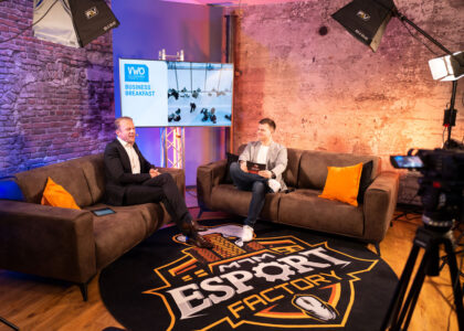 Zwei Männer im Anzug führen ein Gespräch auf braunen Sofas in einem Studio der eSport Factory mit Kamera und Bildschirm.