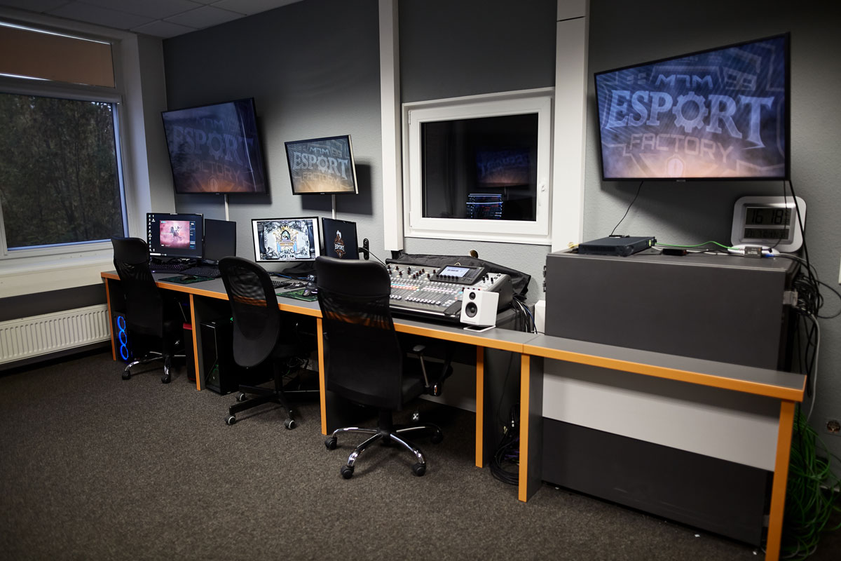 Ein moderner Regieraum mit mehreren Computer-Monitoren, einem Mischpult, Bürostühlen und Screens der eSport Factory.