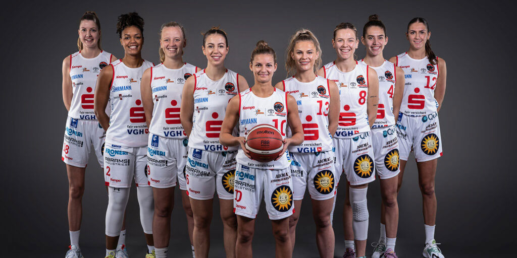 Mannschaftsfoto der Girolive-Panthers Osnabrück: Neun Basketballspielerinnen stehen lächelnd in ihren weiß-roten Trikots nebeneinander; die Spielerin in der Mitte hält einen Basketball.