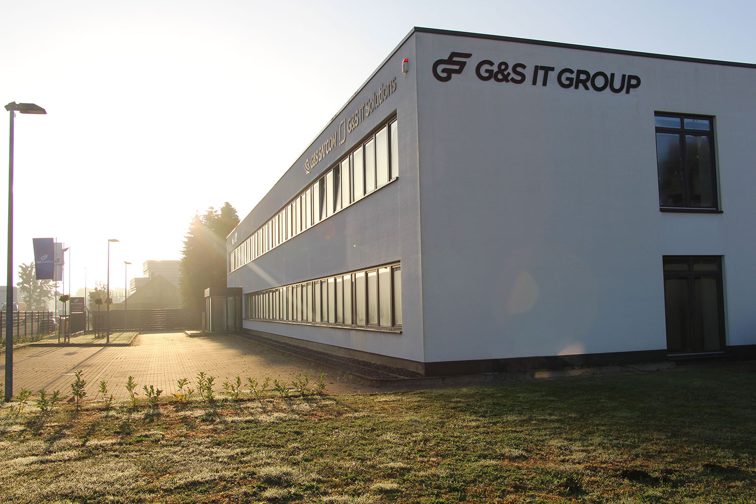 Modernes, weißes Firmengebäude der G&S IT GROUP bei tief stehender Sonne im Gegenlicht.