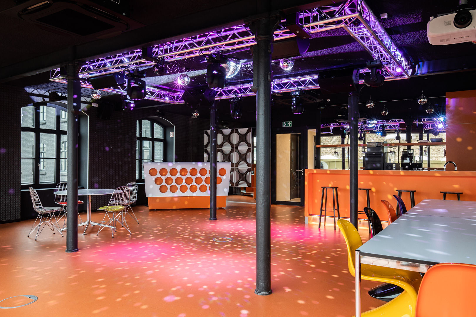 Partyraum mit bunter Beleuchtung, Diskokugeln an der Decke, Theke, Stehtischen und bunten Stühlen.