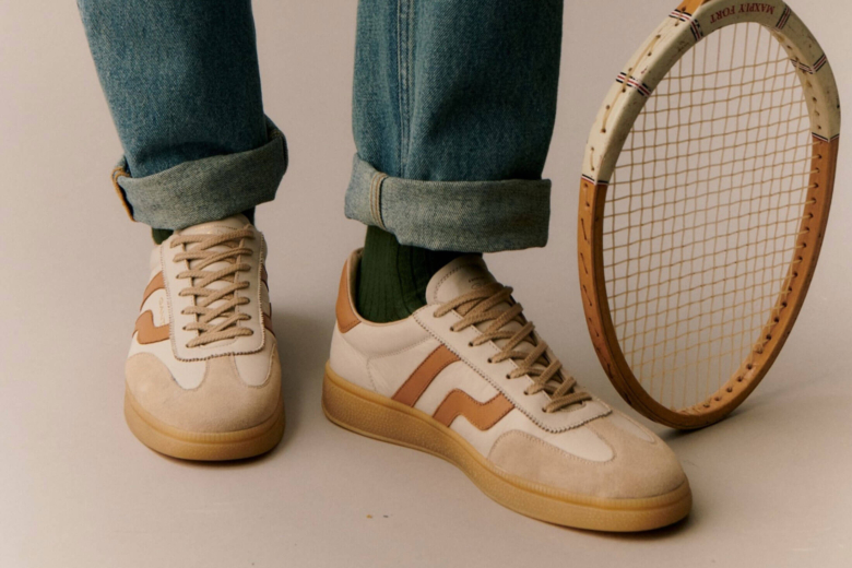 Beine in Jeans und beigefarbenen Sneakern neben einem alten Holz-Tennisschläger