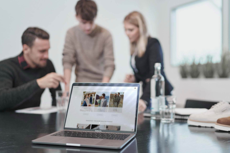 Drei Personen besprechen Arbeitsunterlagen an einem Tisch hinter einem geöffneten Laptop