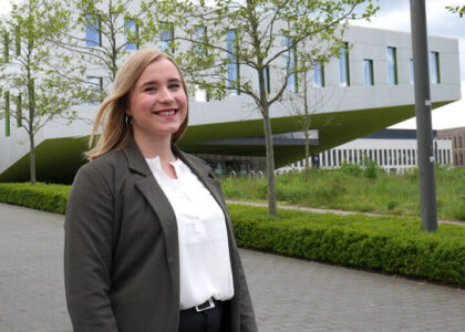 Porträt von Hannah Gensink vor einem modernen, architektonischen Universitäts- oder Bürogebäude im Hintergrund.