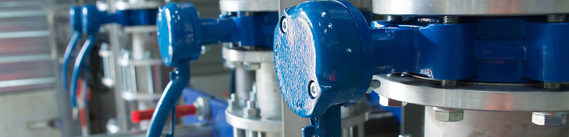 Reihe von blauen Industri Ventilen und metallischen Rohranschlüssen in einer technischen Anlage.