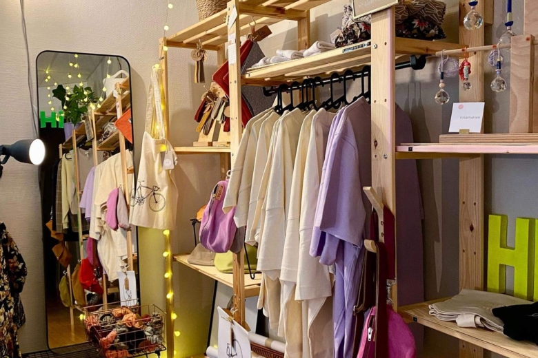Heller Verkaufsraum einer Boutique mit Kleiderstangen aus Holz, aufgehängter Kleidung, Accessoires und Pflanzen.
