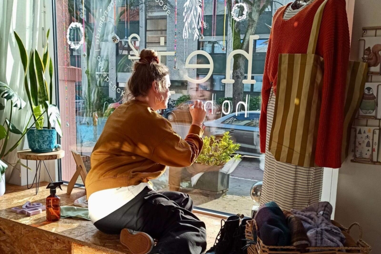 Eine Frau sitzt im Schaufenster eines Geschäfts und bemalt die Scheibe von innen mit weißer Farbe.