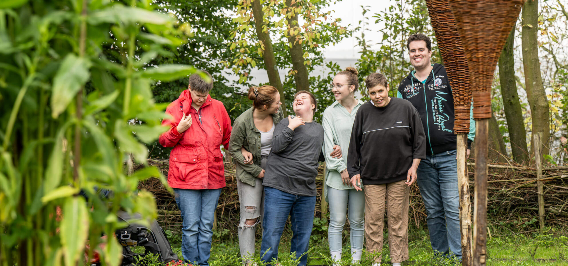 Eine Gruppe von sechs lächelnden Menschen steht zusammen in einem Garten.