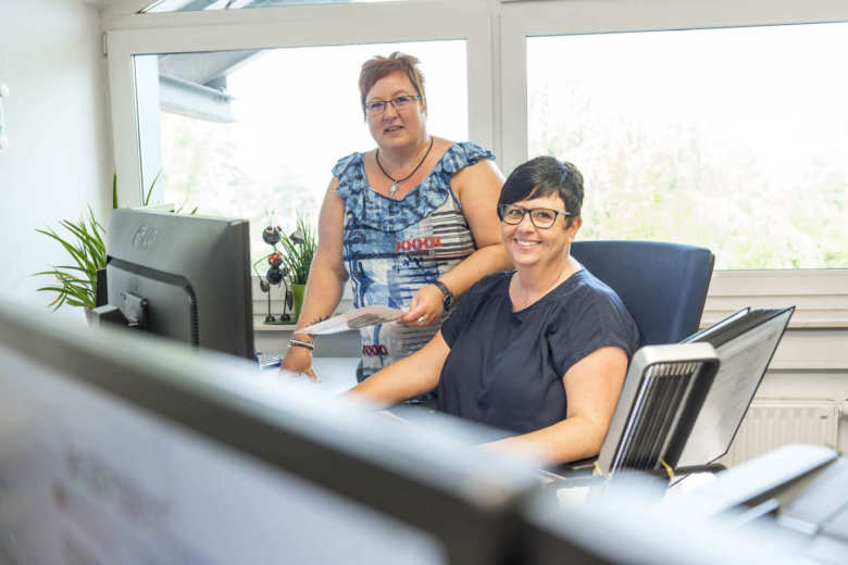Zwei Frauen arbeiten gemeinsam an einem Schreibtisch mit Monitor im Büro.