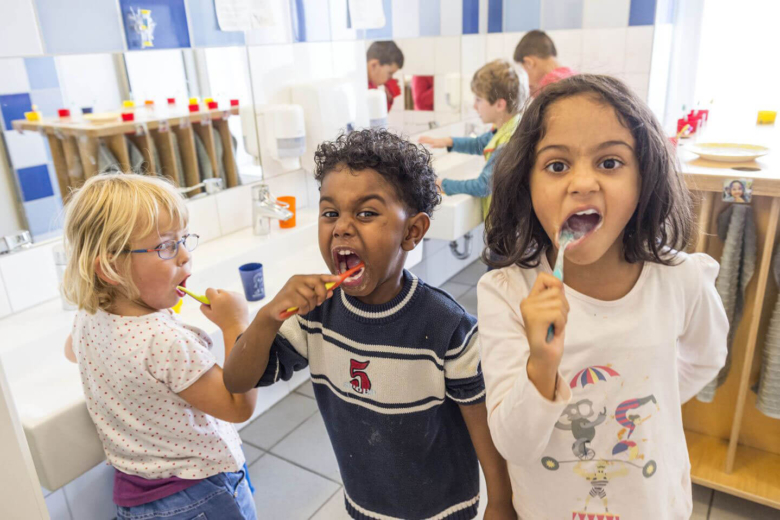 Drei Kinder putzen sich im Badezimmer eines Kindergartens gemeinsam die Zähne.