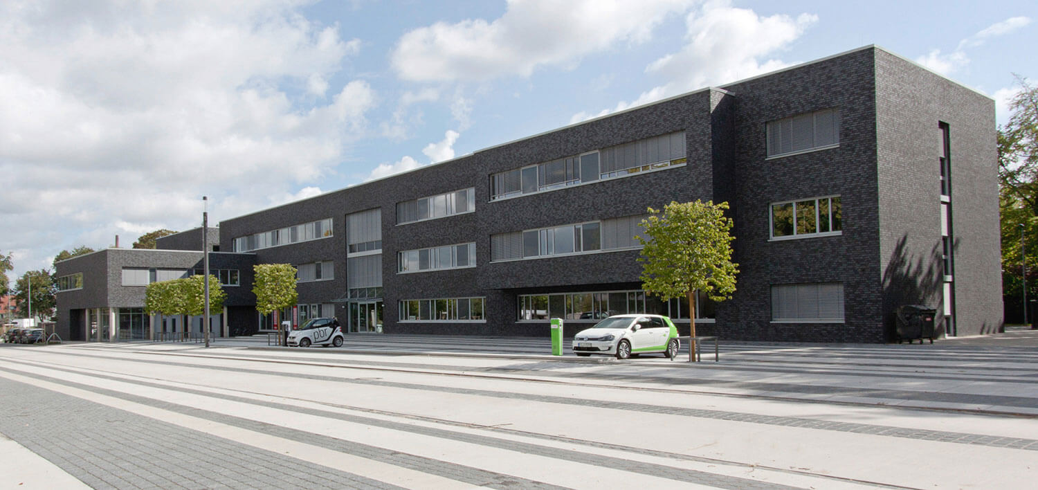 Modernes, dreigeschossiges Bürogebäude mit dunkler Klinkerfassade und gepflastertem Vorplatz.