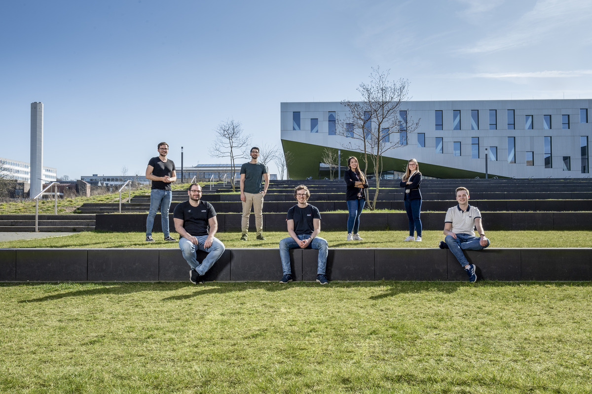 Sieben junge Menschen verteilen sich sitzend und stehend auf den begrünten Terrassenstufen Osnabrücker Hochschulcampus.