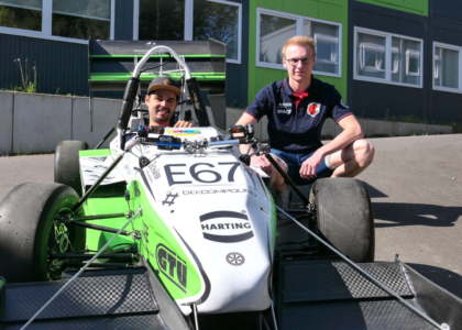 Ein Mann sitzt im grün-weißen Formel-Rennwagen des Ignition Racing Teams, während ein Teammitglied daneben kniet.