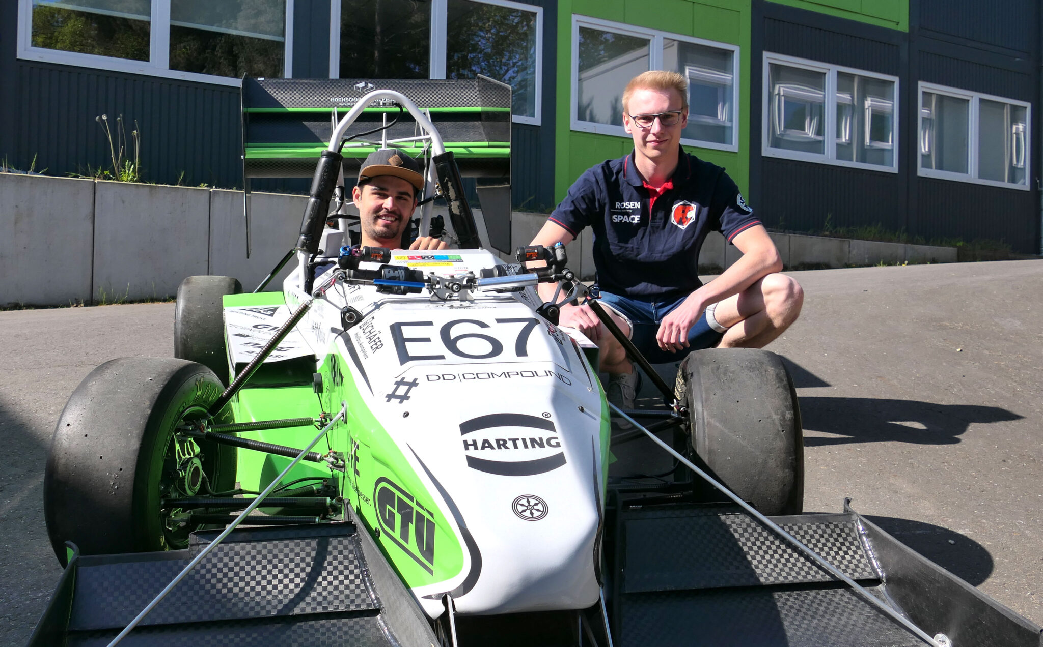 Ein Mann sitzt im grün-weißen Formel-Rennwagen des Ignition Racing Teams, während ein Teammitglied daneben kniet.