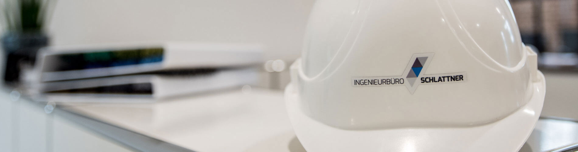 Weißer Bauhelm mit dem Aufdruck Ingenieurbüro Schlattner auf einer Theke.