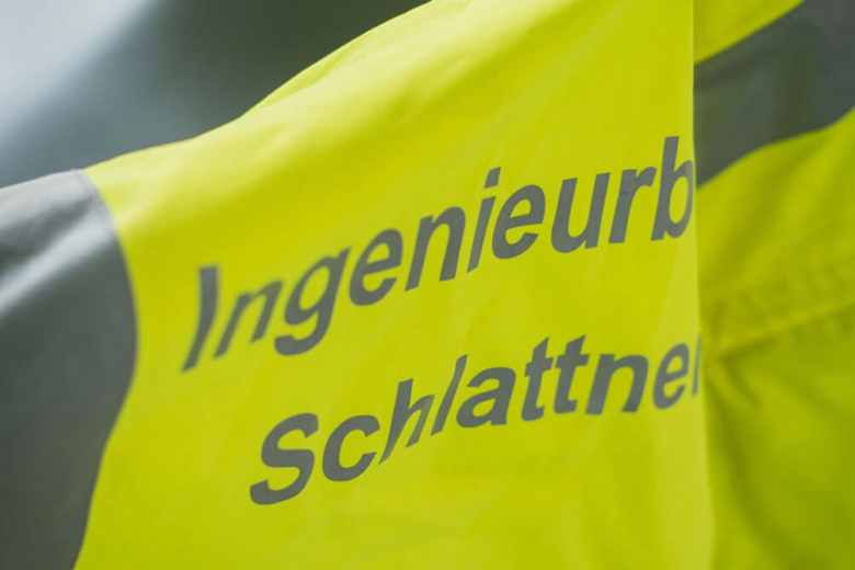 Gelbe Warnweste mit der Aufschrift Ingenieurbüro Schlattner über einer Stuhllehne.