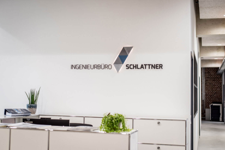 Moderner Empfangsbereich mit Büromöbeln und dem Firmenlogo Ingenieurbüro Schlattner an der Wand.