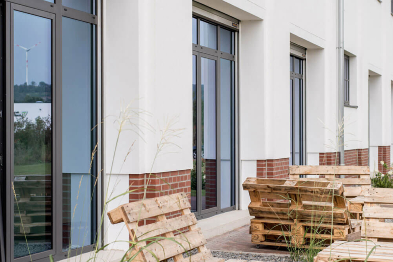 Terrasse mit Holzpaletten-Möbeln vor der Fassade des Bürogebäudes.