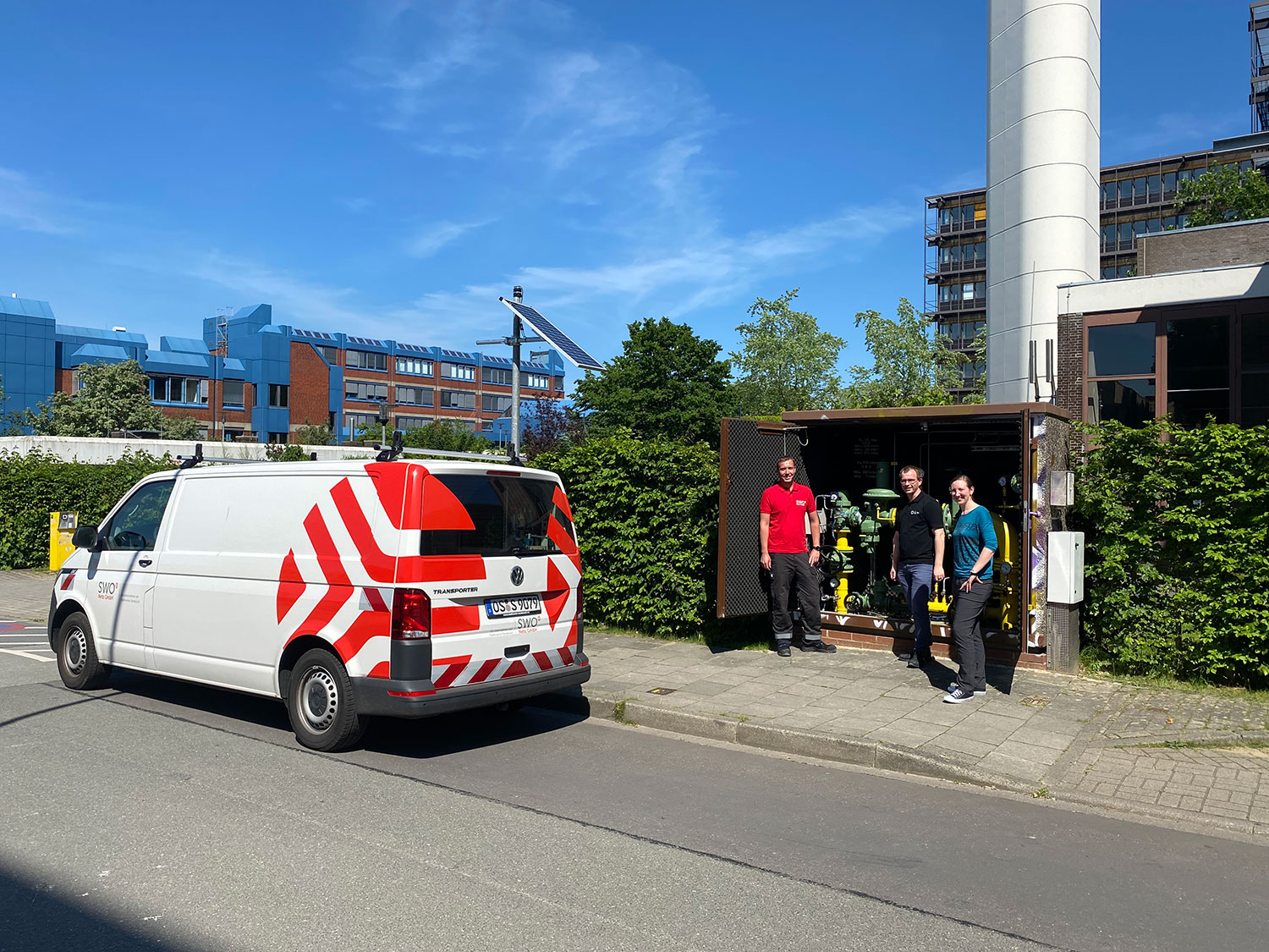 Drei Personen stehen neben einem SWO-Einsatzfahrzeug vor einer geöffneten Gas-Messstation im Freien.