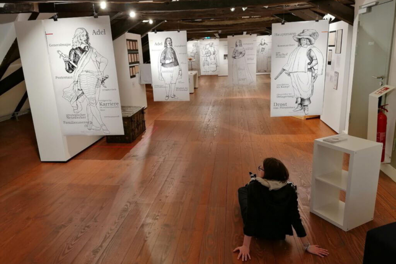udith Franzen sitzt auf dem Boden einer Ausstellungshalle und betrachtet die ausgestellten Exponate.