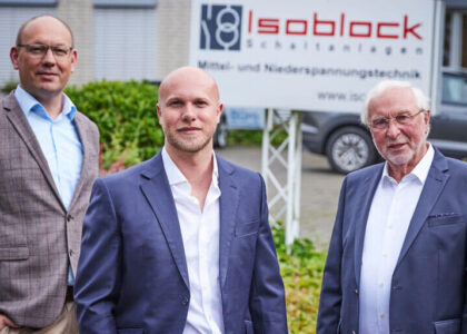 Drei Männer im Anzug bzw. Sakko stehen nebeneinander vor einem Firmenschild von Isoblock Schaltanlagen.
